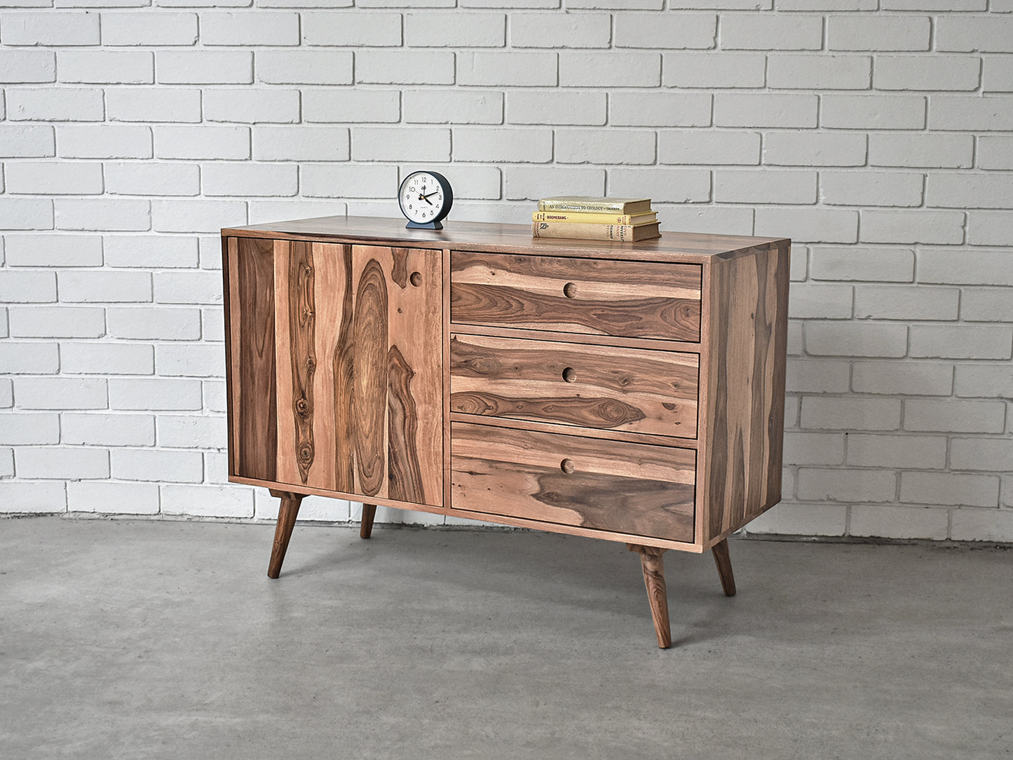 Wooden sideboard with two doors and two drawers against a white brick wall.