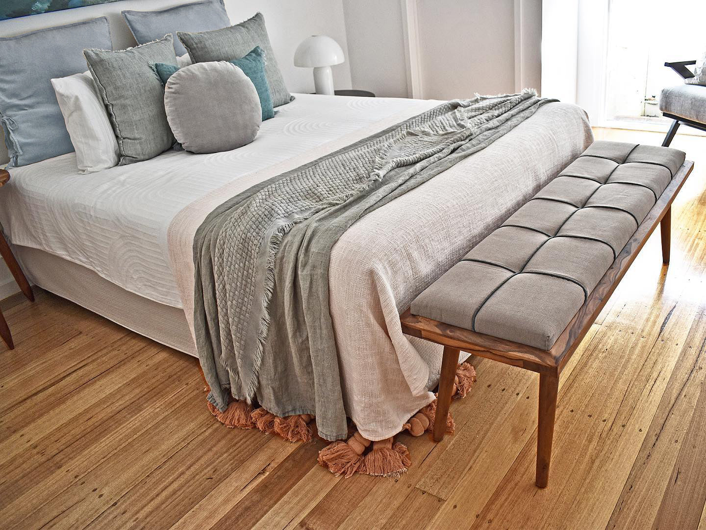 scandinavian light grey padded bench at the foot of a bed 